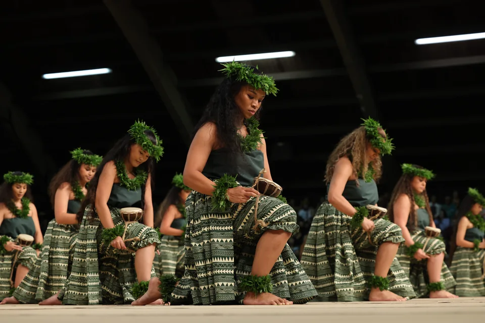 Hālau dancers in green with lei, performing together on stage.